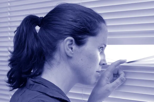 Jovem mulher olhando através de persianas — Fotografia de Stock