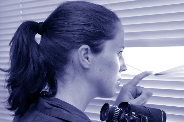 Jonge vrouw op zoek via blinds — Stockfoto