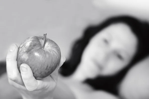 Młoda kobieta leży w łóżku i trzyma jabłko — Zdjęcie stockowe