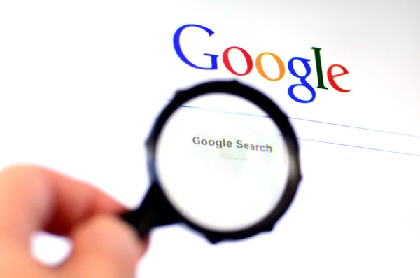 Hand holds Magnifying glass against Google homepage — Stock Photo, Image