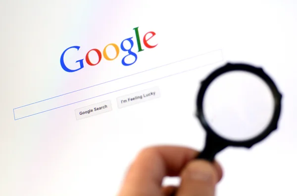 Main tient le verre grossissant contre la page d'accueil Google — Photo