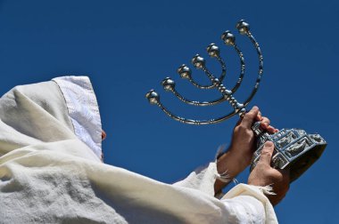 Orthodox Jewish man holding a temple Menorah against clear blue sky. clipart