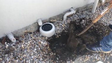 Tesisatçı evin arka bahçesinde su sızıntısı bulmak için büyük bir kürekle çukur kazıyor..
