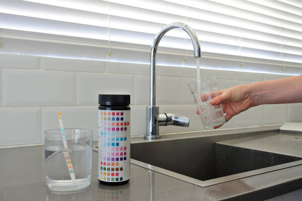 Drinking water test kit on home kitchen counter surface while a person filing a glass cup of tap water.