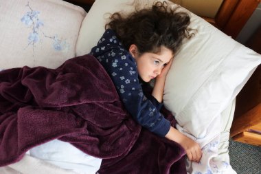 Yatakta yatan üzgün genç kızın (kadın yaş 07-08) havadan bakışı.