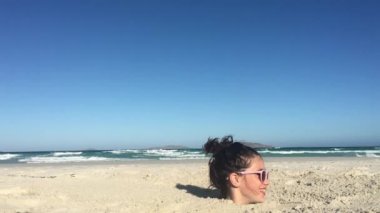 Genç bir kız (11-12 yaş), kumsalda boğazına kadar kuma gömülür. Gerçek insanlar. Boşluğu kopyala