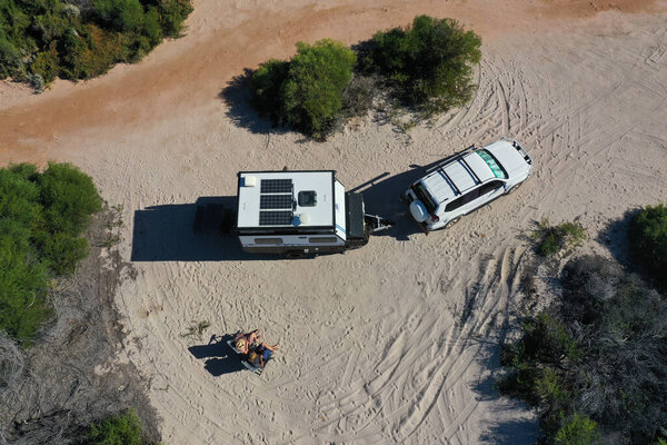 Australian couple relaxing during a beach holiday with 4WD vehicle and caravan on a sand dune in Western Australia outback.