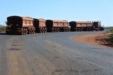 PORT HEDLAND, WA - JUNE 20 2022: Four-trailer road train driving on Great Northern Highway and Newman.Road train is a trucking vehicle used in remote areas of Australia,USA and Europe to move freight efficiently.