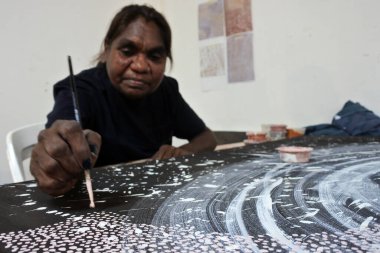 KUNUNURRA, WA - AUG 09 2022:Aboriginal female artist dot painting.Before Indigenous Australian art was ever put onto canvas the Aboriginal people would smooth over the soil to draw sacred ceremony designs.