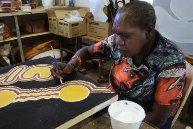 KUNUNURRA, WA - AUG 09 2022:Aboriginal female artist dot painting.Before Indigenous Australian art was ever put onto canvas the Aboriginal people would smooth over the soil to draw sacred ceremony designs.