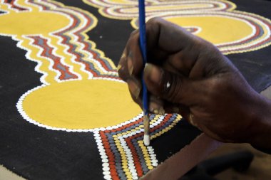 KUNUNURRA, WA - AUG 09 2022:Aboriginal artist hand dot painting.Before Indigenous Australian art was ever put onto canvas the Aboriginal people would smooth over the soil to draw sacred ceremony designs.
