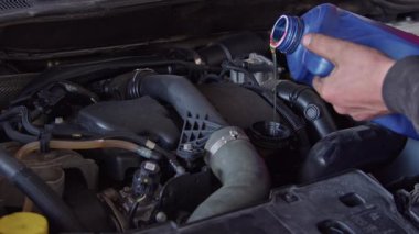 Tamir atölyesindeki arabaya yeni motor yağı dökülüyor.