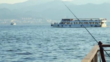 A blue fishing rod resting on the cloudless weather while ferries and boats passing by at the distance on the sea footage.