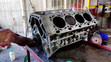 Atölyedeki tamirci araba motorunun silindir bloğunu temizleyip tamir ediyor..