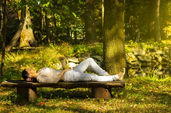 Женщина с закрытыми глазами расслабляется на скамейке на природе — стоковое фото