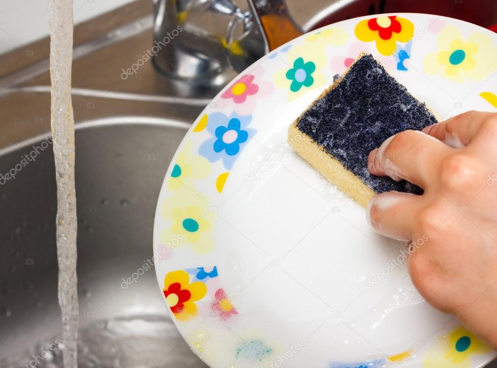 Woman using a yellow sponge to clean the plate