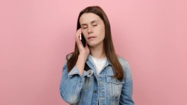 Kafası karışmış, üzgün, 20 'li yaşlarda, üzgün bir kadının portresi cep telefonuyla konuşuyor. Kötü haber ne diye soruyor, mavi kot ceket giyiyor, stüdyodaki pastel pembe arka plan duvarına izole edilmiş şekilde poz veriyor.