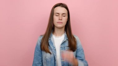 Hasta, yorgun, genç bir kadının portresi 20 'li yaşlarda ellerini başının üstüne koyuyor tapınaklar baş ağrısı çekiyor, migrenden muzdarip, kot ceket giyiyor, pastel pembe stüdyo arka planında izole bir şekilde poz veriyor.