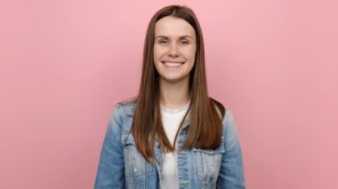 Gülümseyen güzel, doğal, neşeli genç bir kadının portresi sıfır parmak hareketi gösteriyor, kot ceket giymiş, soluk pembe arka plan stüdyosunda izole edilmiş poz veriyor. İnsanların duygu kavramı