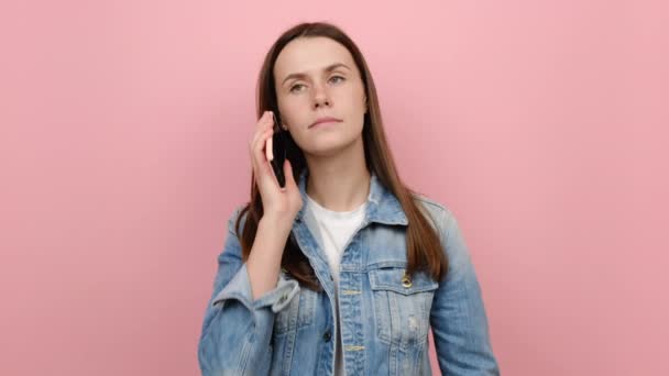 快乐的年轻高加索女人拿着手机说 刚刚发现了重大胜利的消息做得奖的手势 穿着斜纹棉布夹克 在粉色背景工作室里摆出孤立的姿势 — 图库视频影像