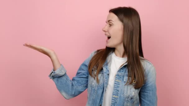 20岁的年轻黑发女人穿着斜纹棉布夹克 手指头放在工作空间上模仿广告商业区 穿着斜纹棉布夹克 隔离在粉红的背景工作室里 — 图库视频影像