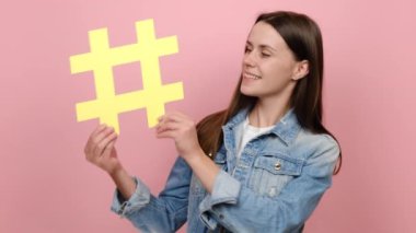 Mutlu 20 'li yaşlarda, dişlek gülüşlü, hashtag sembolü gösteren, kameraya olumlu bakan, ünlü blog' u etiketleyen, virüs içerikli, kot ceket giyen, pembe stüdyo geçmişine izole edilmiş genç bir kadın.