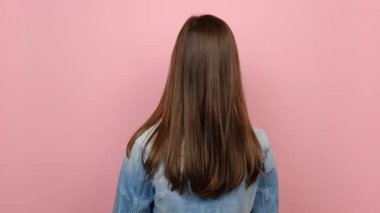 Arkaya bakan mutlu genç yirmili yaşlardaki kadın kameranın etrafında dönüyor jest gibi başparmak gösteriyor, kot ceket giyiyor, pastel pembe arka planda izole edilmiş poz veriyor. En iyi seçim konsepti
