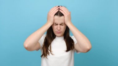 Stresli, sağlıksız, bin yıllık esmer kız migren, panik atak ve yüksek tansiyon yüzünden yorgun hissediyor. Hüsrana uğramış genç bir kadın, baş şakaklarına masaj yapıyor, mavi arka planda poz veriyor.