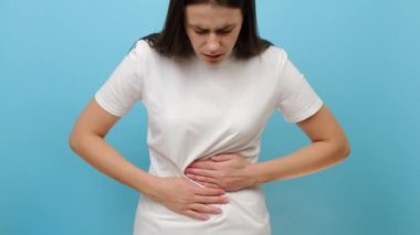Üzgün genç bir kadın mide ağrısı çekiyor. Mavi arka plan stüdyosunda izole edilmiş. Milenyum dişisi mide ağrısı çekiyor. Karın bölgesinde şiddetli ağrı ve kramp var. Adet görme.
