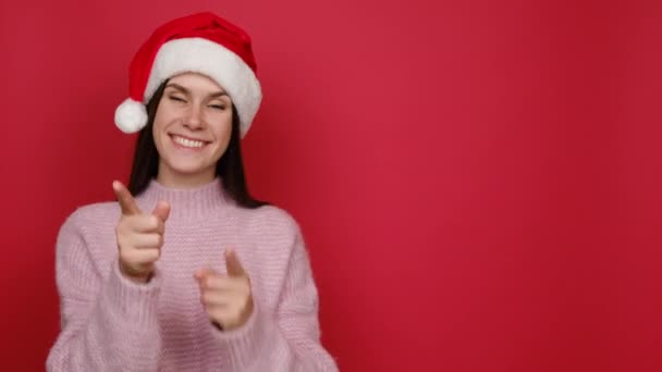 身着粉色毛衣 头戴圣诞帽的年轻圣诞老人20多岁的画像手拉手放在工作空间上 模仿商业区 在红色的工作室背景下被隔离 新年概念 — 图库视频影像