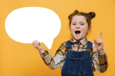 Happy 'nin elinde konuşma balonu tutan çocuk parmağını kaldırdı, iyi fikir, kameraya olumlu baktı, gömlek giydi, stüdyoda sarı arka plan duvarının üzerine izole edilmiş pozlar verdi.
