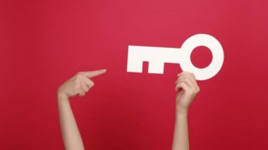 Kadın elinin büyük beyaz anahtarıyla parmaklarıyla ok işareti yapıyor, mükemmel bir sembol, kırmızı renk arka plan stüdyosu üzerinde izole edilmiş ve içeriği için fotokopi alanı var. Kira, emlak kavramı