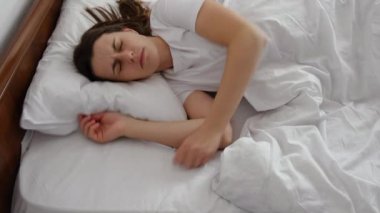 Rahatsız bir yatakta yuvarlanan, kötü yatak ve çarşaflardan rahatsız olan, uykusuzluk sorunu yaşayan, uykusuzluk çeken, uykusuzluk çeken, uyuyamayan genç bir kadının yan görüntüsü.