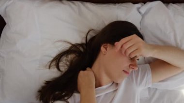 Yorgun ve esmer bir kadının sabah uyandıktan sonra yatakta uzanmış kaslarını esnetip sert omuz kaslarını ovmasının en güzel görüntüsü. Kötü yatak ya da duruş sorunları yüzünden üzgün kız kendini rahatsız hissediyor.