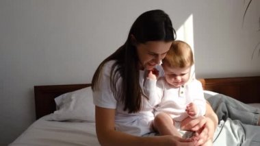 Sevecen, sevgi dolu, genç bir anneye yakın tatlı, küçük bir kız çocuğuyla güzel bir anın tadını çıkarıyor. Evdeki rahat beyaz yatakta oturuyor. Mutlu bir beyaz anne, gülen küçük bir bebekle vakit geçiriyor.