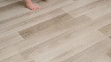 Çıplak ayaklı bir kızın sıcak zeminde yürümeyi öğrenmesini yakından izleyin. Güzel bebek adımları. Yeraltı ısıtma konsepti