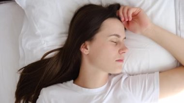 Sakin, genç bir bayanın rahat, temiz bir yatakta, yumuşak yastıkta, beyaz keten ortopedik yatakta, huzurlu 20 'li yaşlarda, uykusunda dinlenen, sağlıklı, güzel bir uyku uykusunun keyfini çıkardığı bir manzara.