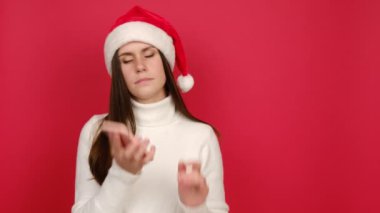 Genç ve tatlı bir bayan cep telefonuyla konuşarak beyaz kazak ve Noel şapkası giyer. Tebrikleri kabul eder ve kırmızı arka plan duvarında izole bir şekilde poz verir. Mutlu yıllar, mutlu noeller.