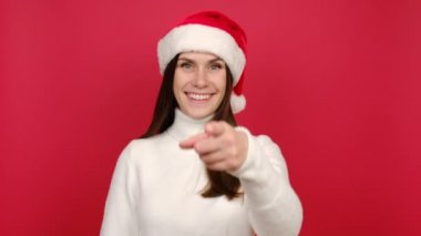 Beyaz kazaklı ve Noel Baba şapkalı mutlu genç kadın kırmızı arka plan stüdyosunda yalnız poz vererek beni ara diyor. Mutlu yeni yıl kutlamaları, mutlu tatiller.