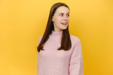 Gülümseyen meraklı öğrenci, sevimli, çekici, pembe örgü süveter giyen, sarı arka plan stüdyosunun üzerinde yalnız poz veren, şaşırtıcı bir şekilde şaşırmış öğrenci. Duygu kavramı