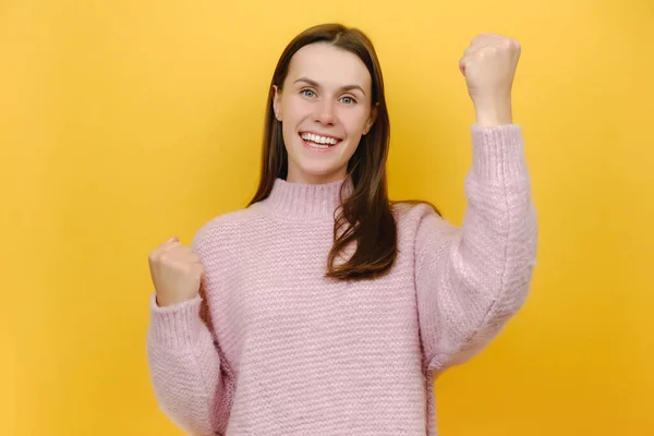 快乐的成功喜庆的幸运儿漂亮的年轻漂亮的20多岁的女子做得奖的手势握紧拳头庆祝 穿着针织毛衣 被隔离在工作室黄色的背景墙上 — 图库照片