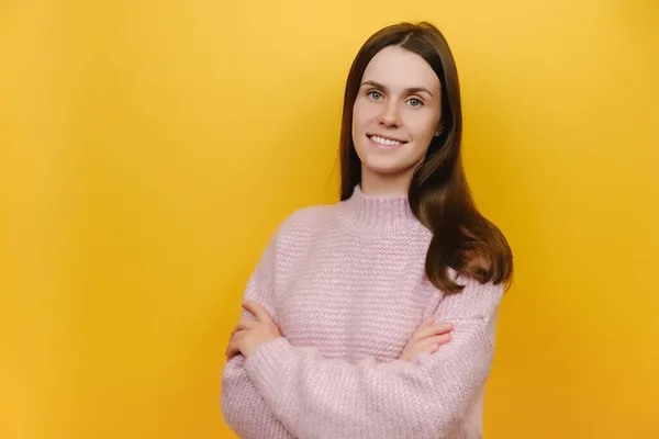 侧面看去 笑容满面的快乐年轻的高加索女人 身穿粉色针织毛衣 手挽手交叉 在工作室的黄色背景墙上显得孤立无援 人的生活方式概念 — 图库照片
