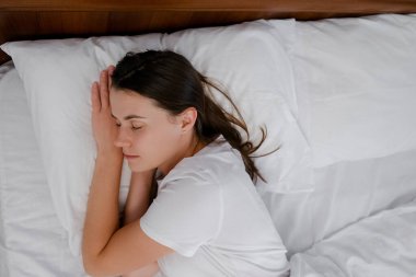 Sakin, genç, beyaz, 20 'li yaşlarda bir kadının rahat, rahat, taze, beyaz bir yatakta uyuyup sağlıklı, güzel bir uyku uykusunun tadını çıkarmasının üst görüntüsü. Çekici milenyum hanımı uyumaya gidiyor.