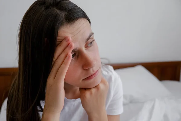 闷闷不乐的女人在床上坐着醒来感觉到压力焦虑 睡不好后梦魇的概念独自坐在卧室里 忧心忡忡的黑发女人在早晨失眠 有选择的重点 — 图库照片