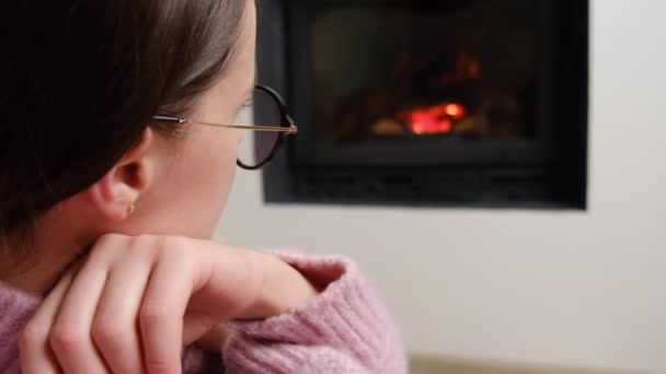 年轻的黑发女子坐在壁炉旁温暖的地板上 选择性地聚焦在眼镜上 享受着现代乡村村舍平静的周末 冬季和假期的概念 — 图库视频影像