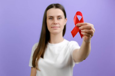 Genç dişinin seçici odak noktası elinde kırmızı kurdele tutarak kameraya mor arka planda poz veriyor. AID 'ler, tedavi önleme ve koruma, hayır kurumunda gönüllü destek. Dünya göğüs kanseri günü