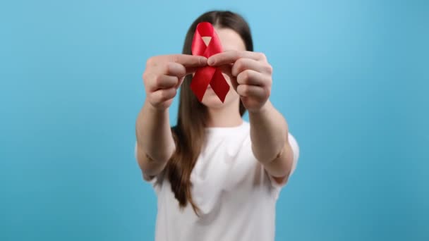 年轻女孩的选择性焦点手握红丝带 在镜头前展示 模仿蓝色背景 Aids治疗 预防和保护 志愿慈善支助 世界乳腺癌日 — 图库视频影像