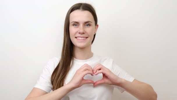Smiling young female volunteer showing hands sign heart shape looking at camera, posing over white wall. Healthy heart health life insurance, love and charity, voluntary social work, donation concept