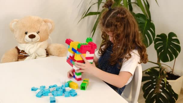有魅力的孩子喜欢游戏时间 用五彩缤纷的建材砌成的砖 周末休闲活动的概念 白人女孩坐在舒适的客厅的桌旁 玩着塑料立方体和毛绒玩具熊 — 图库视频影像
