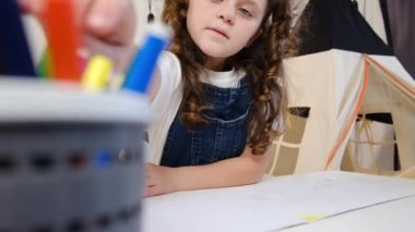 Tek başına oynayan sevimli kız ressamın seçici odak noktası keçeli kalemle resim çizmesi masaya oturması, okul çocuğunun evde yaratıcı sanat hobisinin keyfini çıkarması. Çocuk gelişimi kavramı